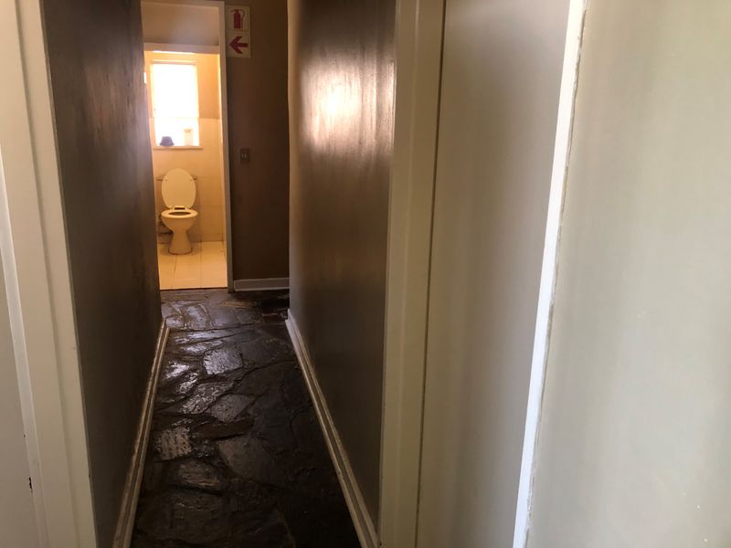 A narrow hallway featuring rustic stone flooring leading towards a separate bathroom area with a toilet.