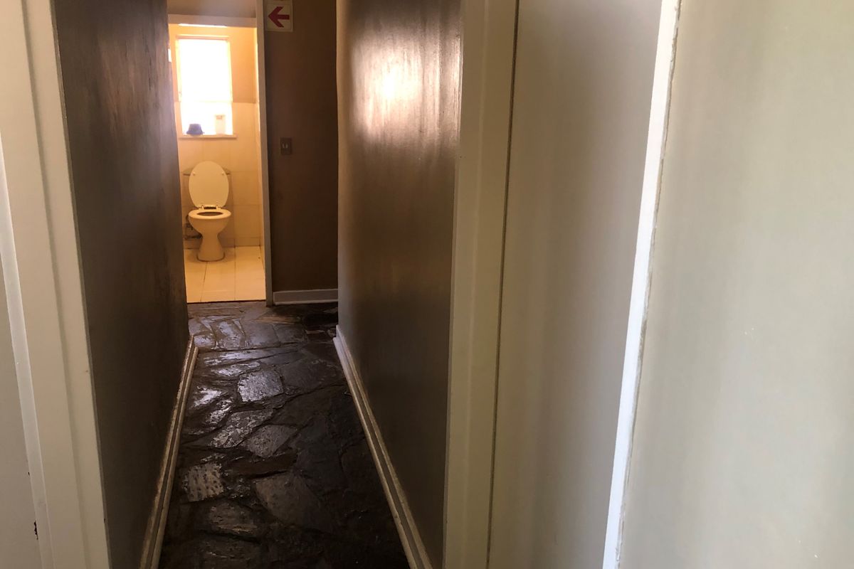 A narrow hallway featuring rustic stone flooring leading towards a separate bathroom area with a toilet.