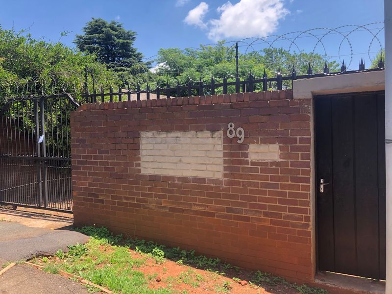 Front boundary wall featuring brick construction, security gate, and pedestrian access door with visible patch repairs on the masonry.