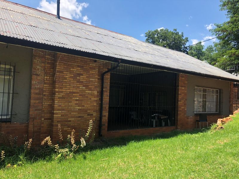 Rear view of the house featuring a corrugated metal roof, face brick exterior, and a covered patio area secured with metal bars.