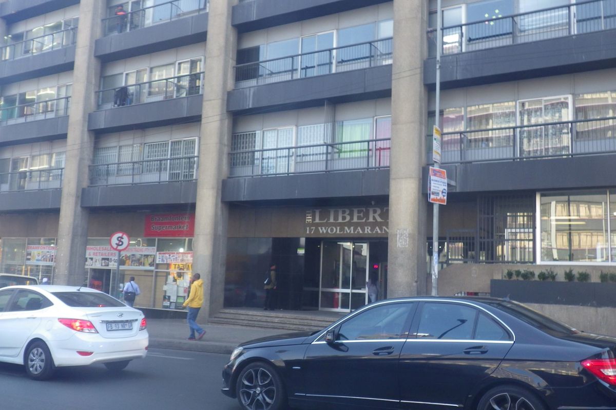 Street-level view of the front facade of The Liberty apartment building, featuring ground floor retail spaces and residential balconies above.