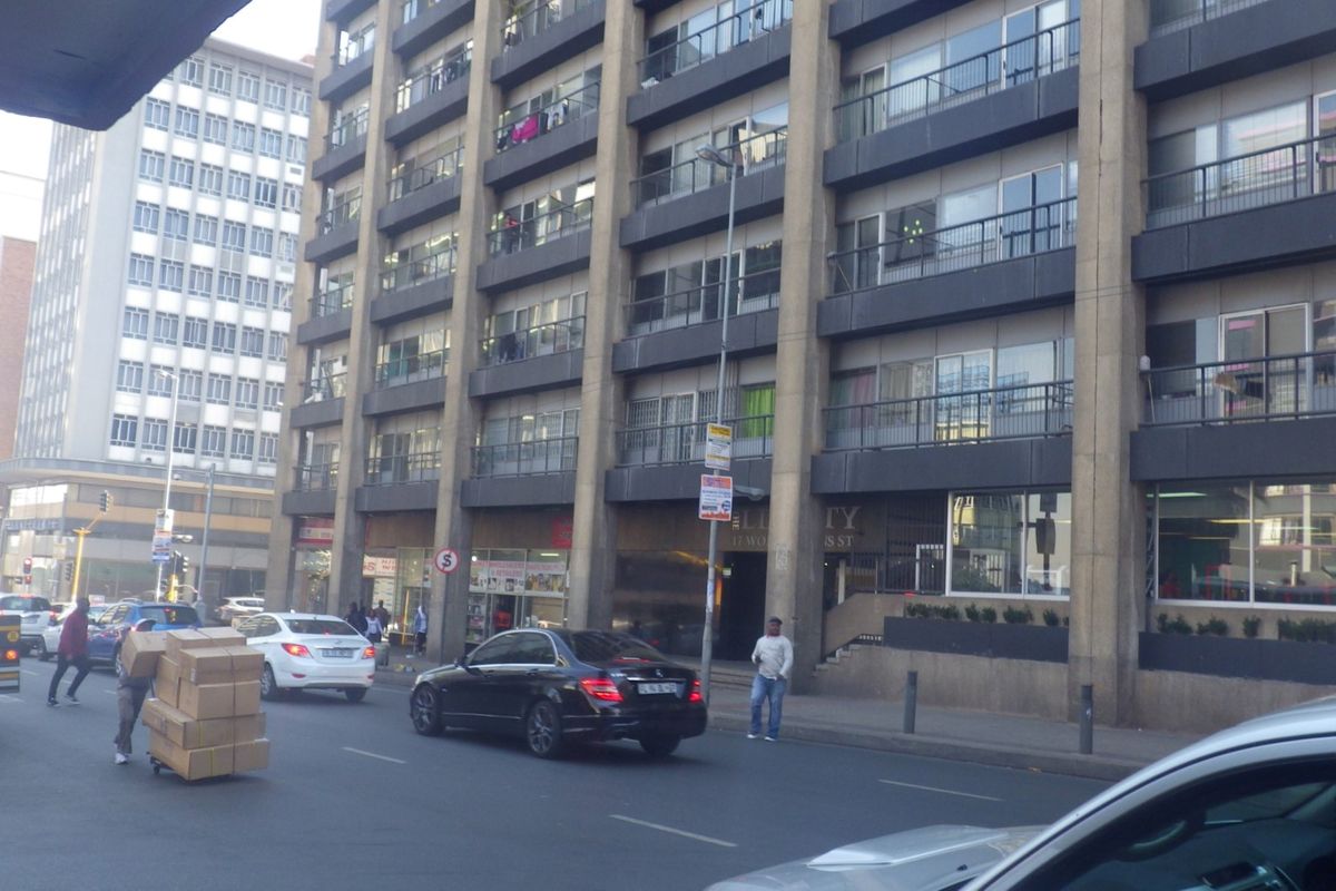 Street-level view of a multi-story apartment building featuring concrete architecture, private balconies, and ground-floor commercial space in an urban setting.
