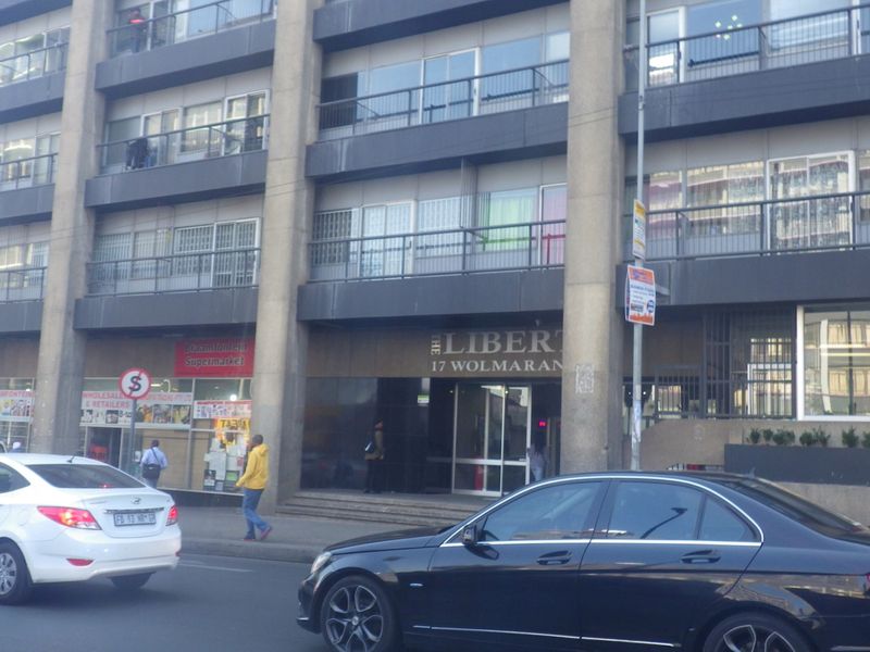 Street-level view of the front facade of The Liberty apartment building, featuring ground floor retail spaces and residential balconies above.