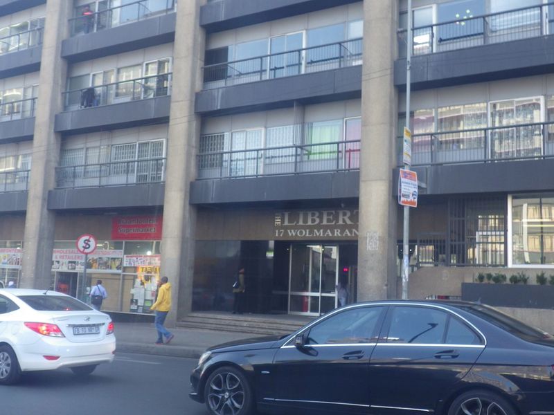 Street-level view of the front facade of The Liberty apartment building, featuring ground floor retail space and residential balconies above.