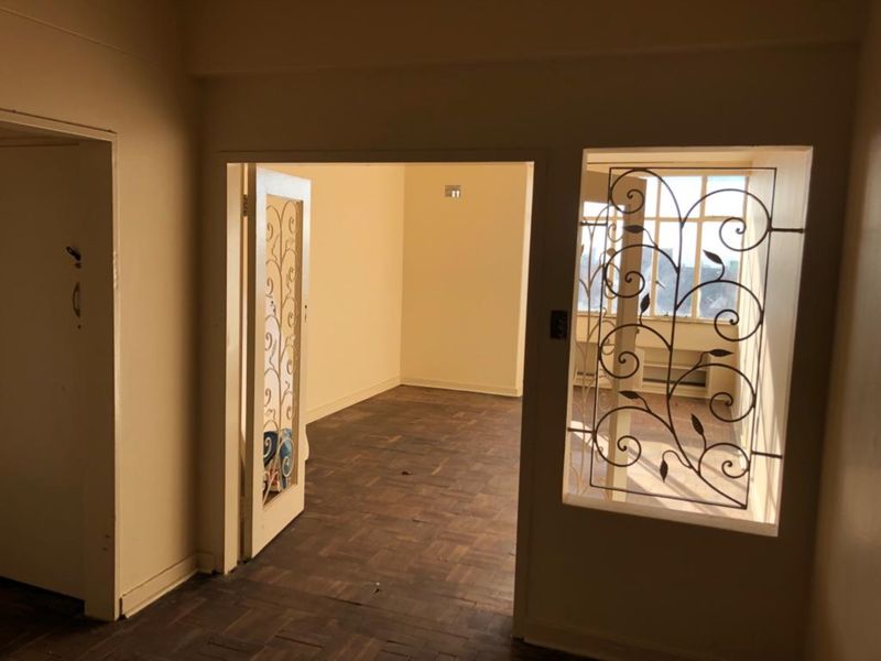 An empty living area featuring original parquet flooring and a decorative wrought iron security screen, offering a blank canvas for renovation.