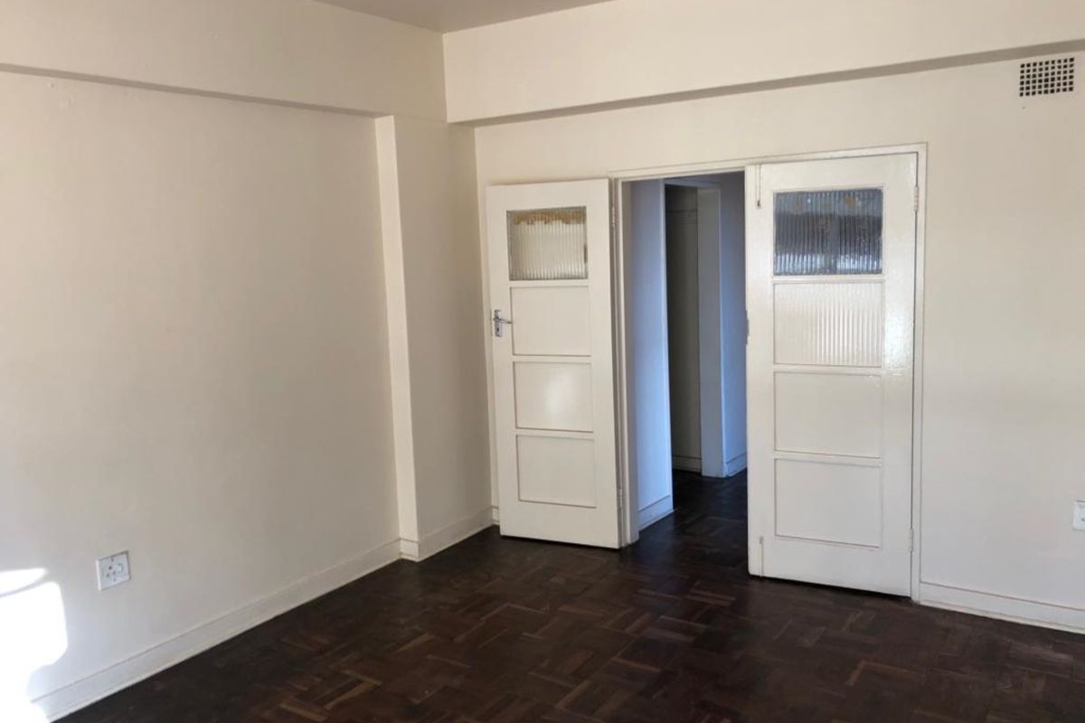 An empty living room featuring original parquet flooring and classic double doors leading to an adjacent space.