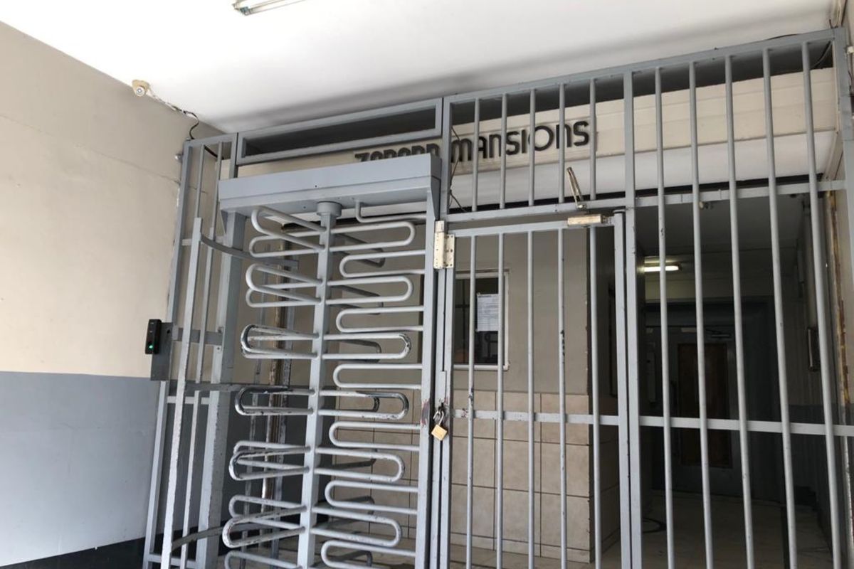 Building entrance featuring a secure metal turnstile and gate system with access control, providing a functional entry point to the apartment complex.