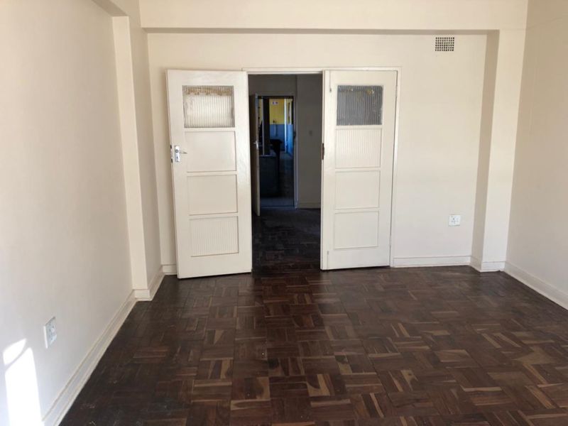 An empty living room featuring original parquet flooring and double doors leading to an adjacent space.