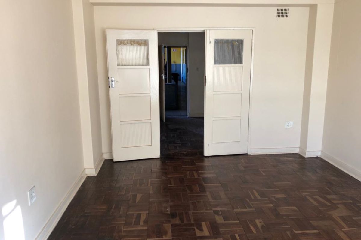An empty living room featuring original parquet flooring and double doors leading to an adjacent space.