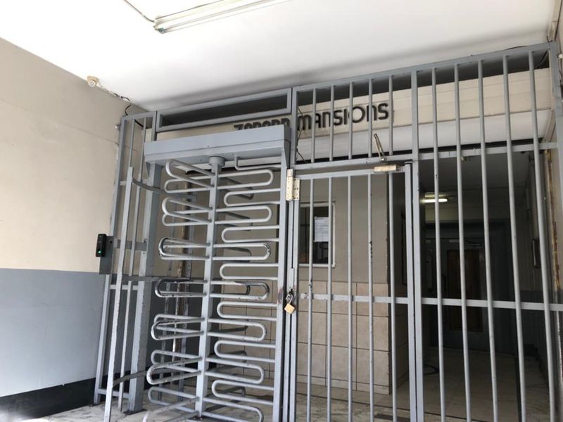 Building entrance featuring a secure metal turnstile and gate system with access control, providing a functional entry point to the apartment complex.