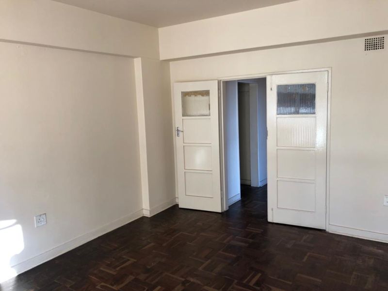 An empty living room featuring original parquet flooring and classic double doors leading to an adjacent space.