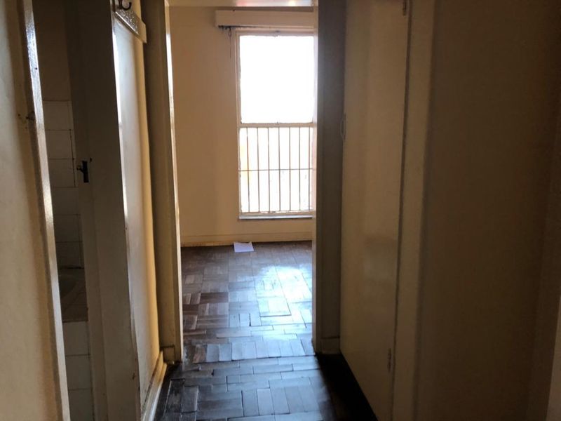 A vacant hallway featuring parquet flooring, built-in storage cupboards, and a window fitted with security bars.
