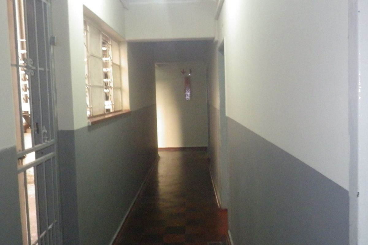 A narrow interior hallway featuring parquet flooring, security gate, and two-tone wall paint, providing access to various rooms within the property.