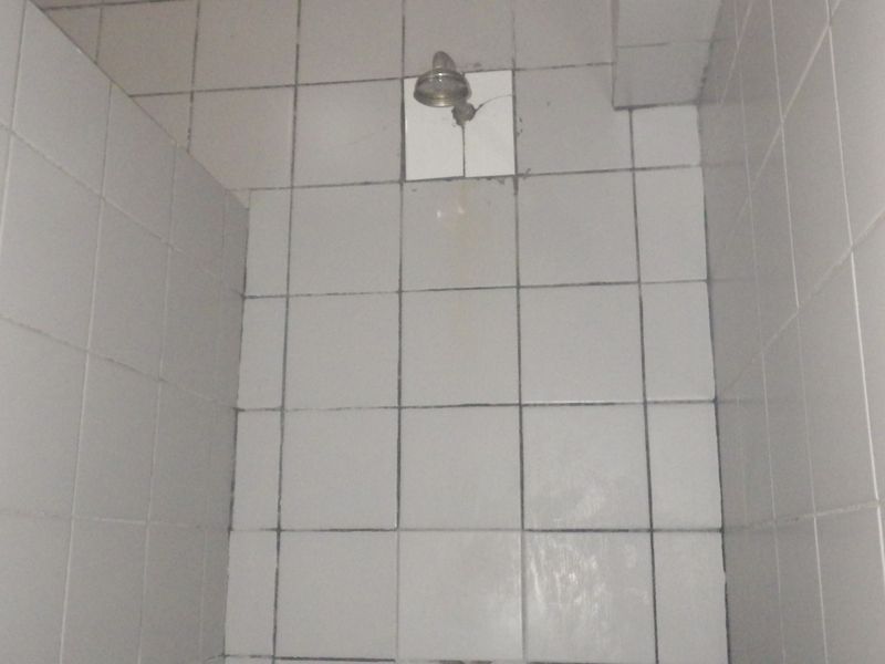 A basic shower enclosure featuring white ceramic wall tiles and a standard shower head, requiring cosmetic updates to improve its condition.