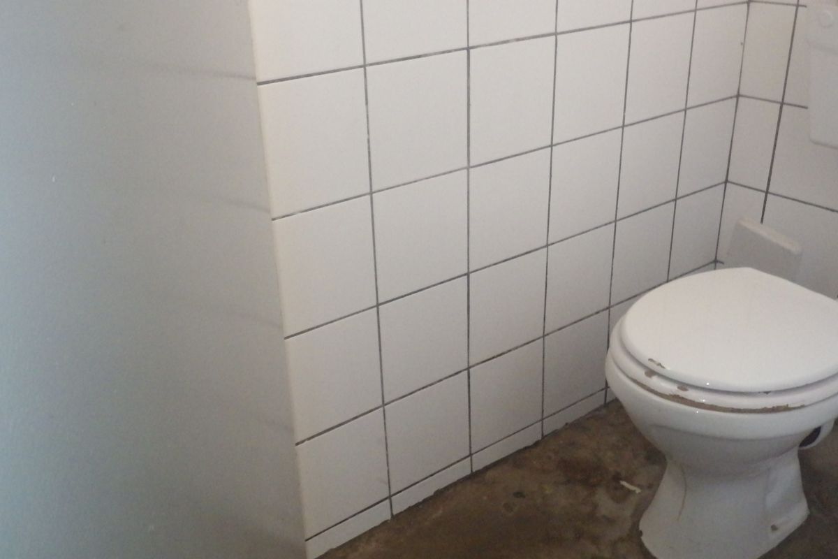 A small bathroom featuring white ceramic wall tiles and a standard toilet, currently requiring cosmetic updates and floor finishing.