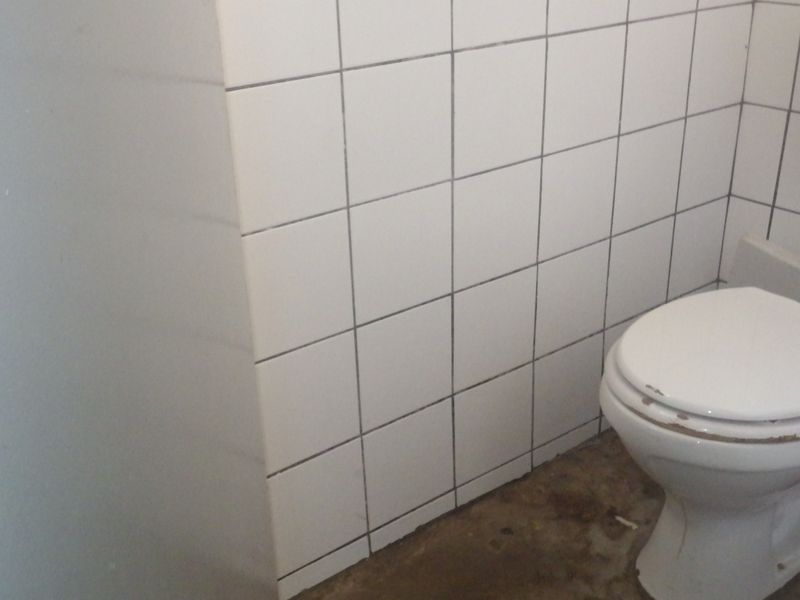 A small bathroom featuring white ceramic wall tiles and a standard toilet, currently requiring cosmetic updates and floor finishing.