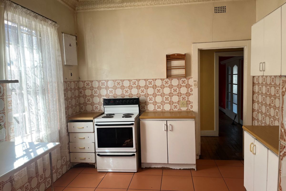 A dated kitchen featuring original patterned wall tiles, terracotta floor tiles, built-in cabinetry, and a freestanding electric stove.