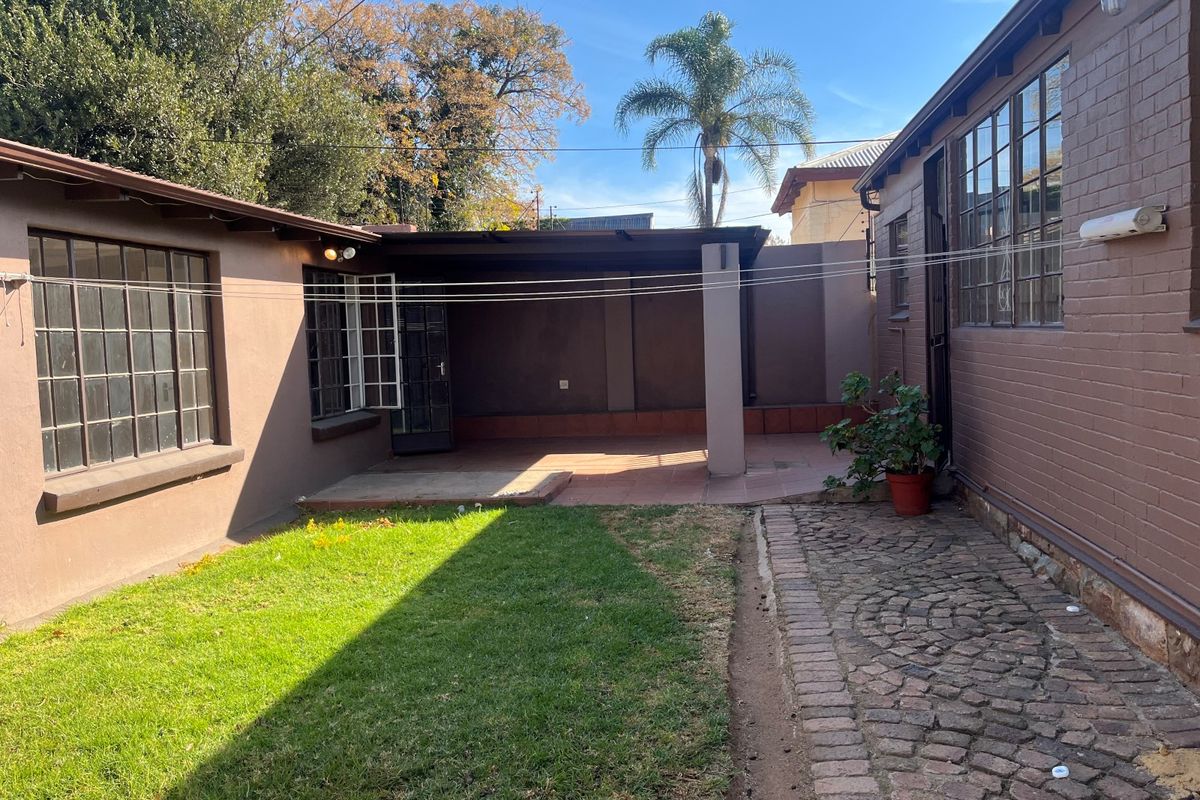 Rear exterior view featuring a covered patio area, cobblestone paving, and a small lawn space adjacent to the main dwelling.