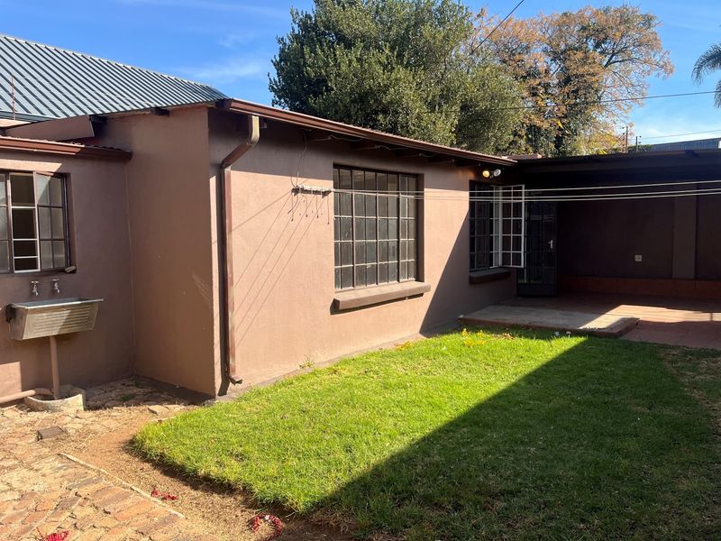 Rear exterior view of the property featuring a small lawn, covered patio area, steel-framed windows, and an external utility sink.
