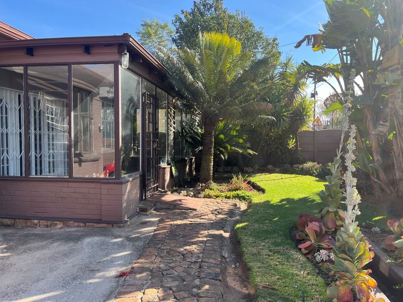 A rear garden view featuring a paved walkway leading to an enclosed patio area, surrounded by established landscaping and a secure boundary wall.