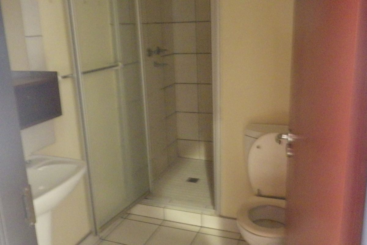A functional bathroom featuring a walk-in shower enclosure, pedestal basin, and toilet, with tiled flooring and walls.