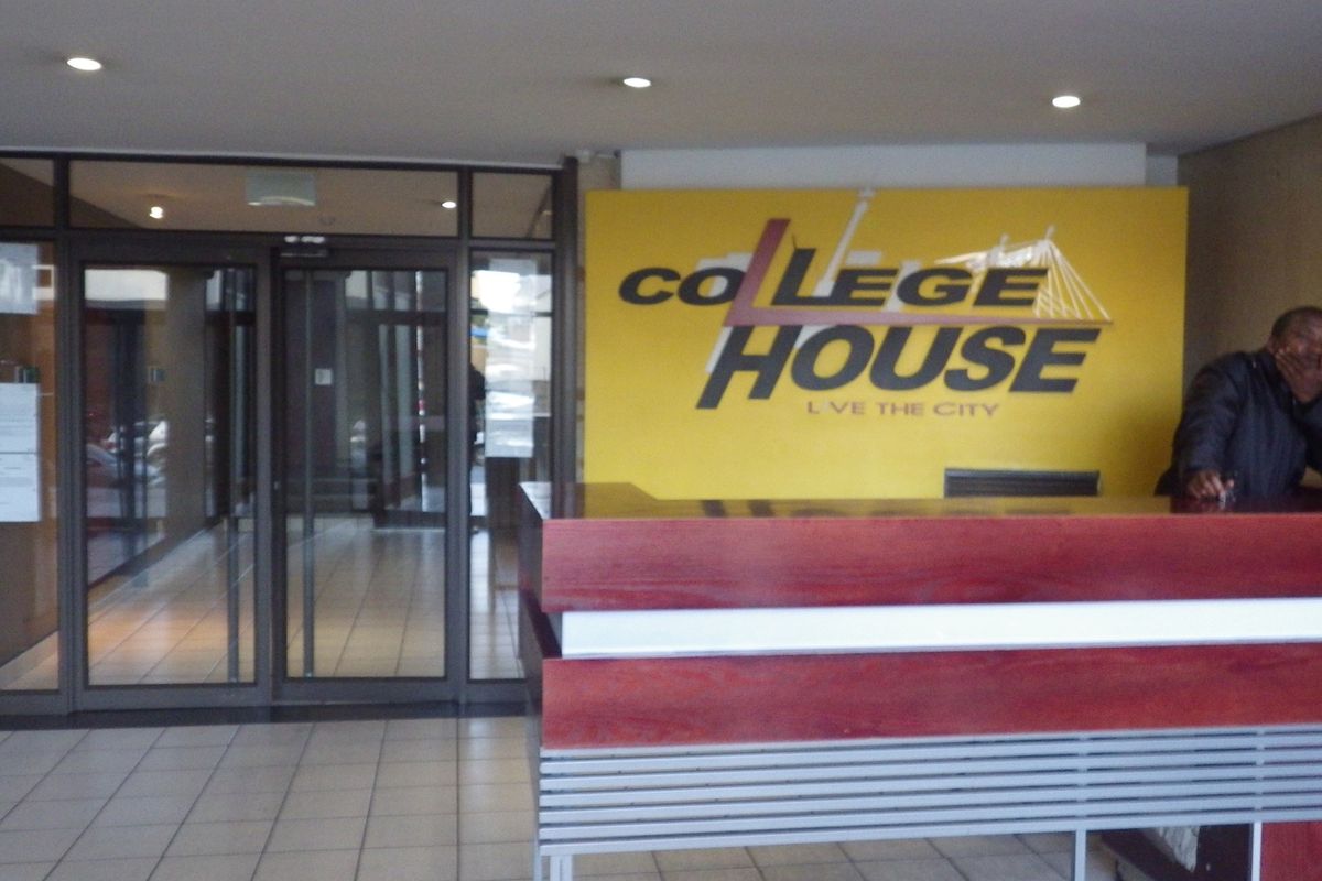 A reception area featuring a built-in wooden reception desk, tiled flooring, and glass entrance doors.
