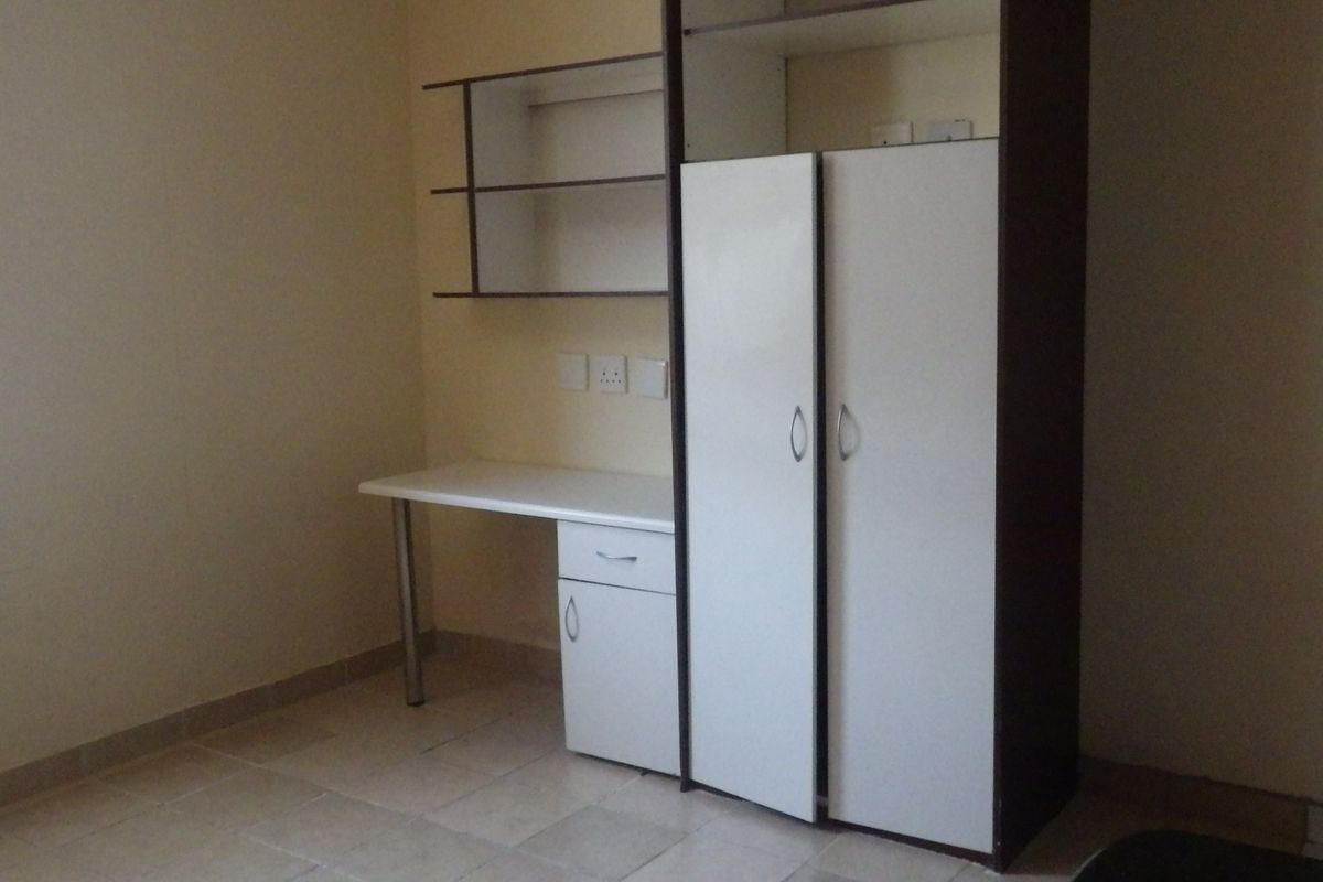 A bedroom featuring built-in cabinetry, including a desk area with shelving and a wardrobe, set against a neutral backdrop with tiled flooring.