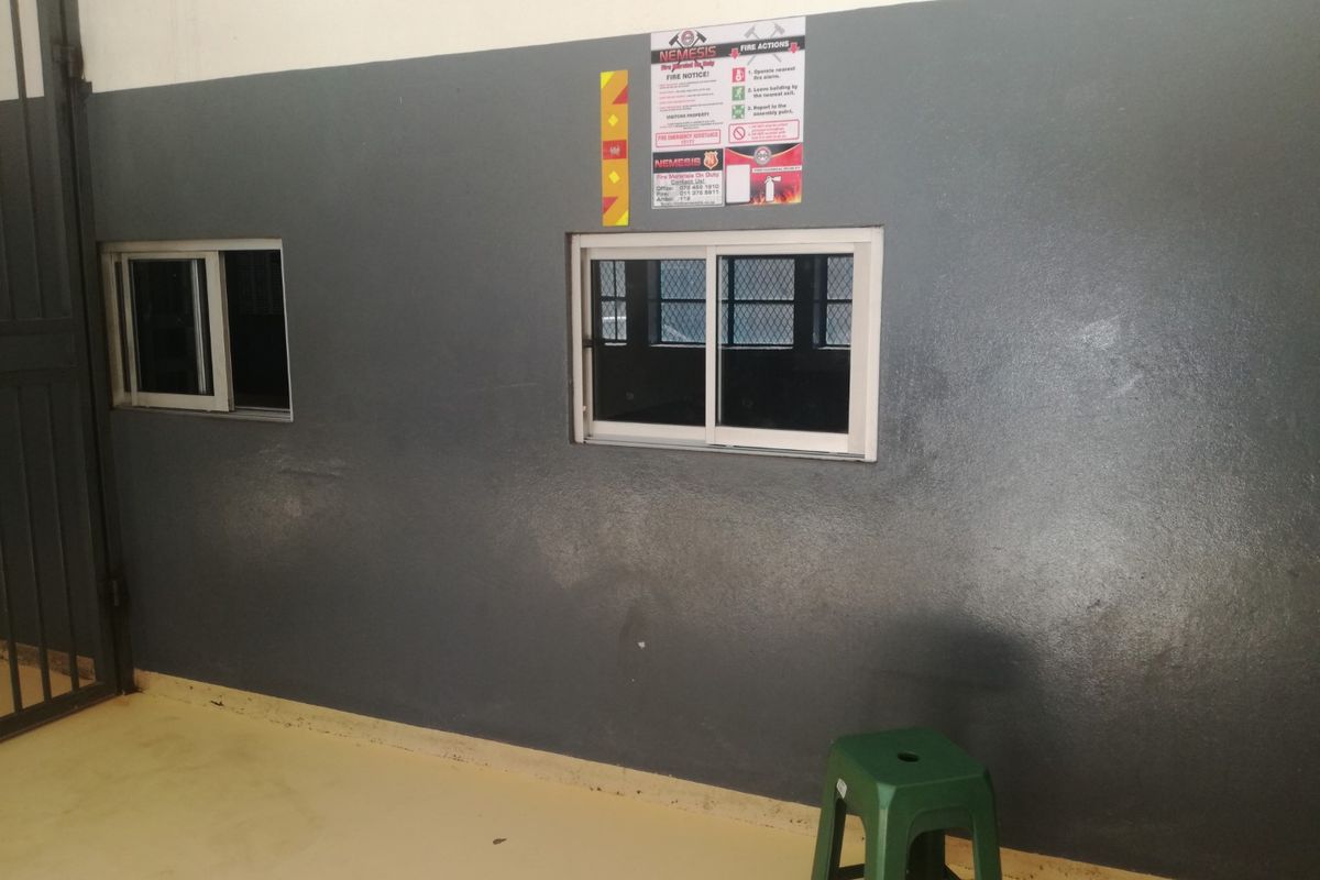 A functional utility space featuring painted walls, sliding windows, and a security gate, suitable for various storage or operational purposes.