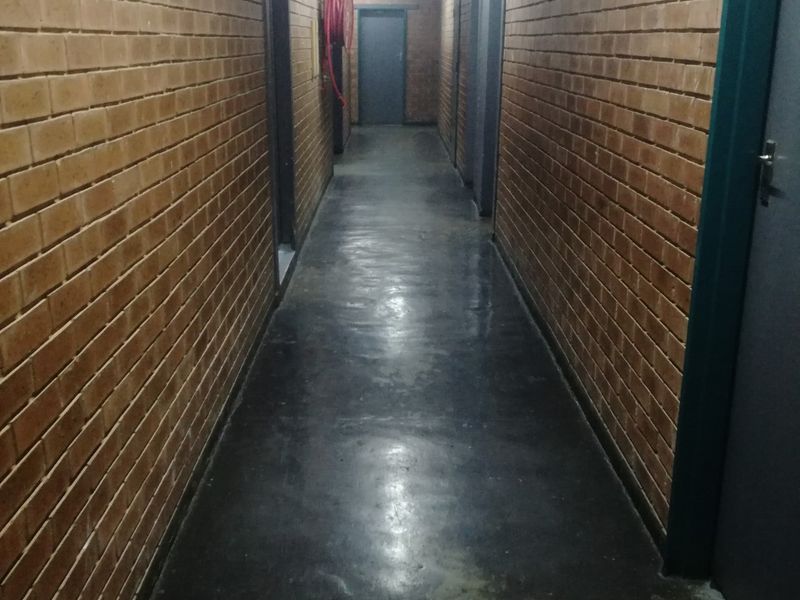 A long, industrial-style hallway featuring exposed brick walls, painted concrete flooring, and integrated emergency safety equipment.
