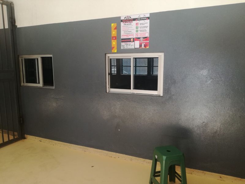 A functional utility space featuring painted walls, sliding windows, and a security gate, suitable for various storage or operational purposes.