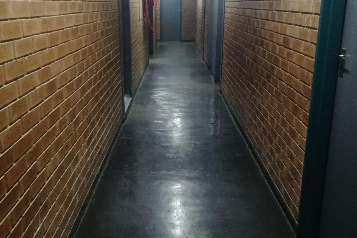 A long, industrial-style hallway featuring exposed brick walls, painted concrete flooring, and integrated emergency safety equipment.