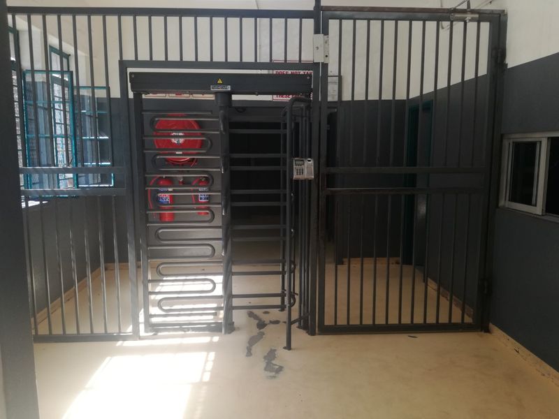 A secure utility access area featuring a turnstile, metal security gates, access control keypad, and fire safety equipment.