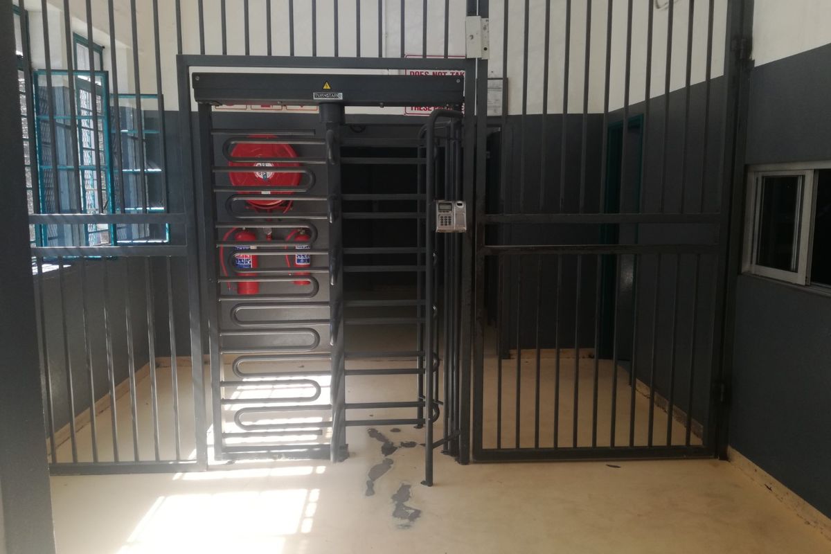 A secure utility access area featuring a turnstile, metal security gates, access control keypad, and fire safety equipment.