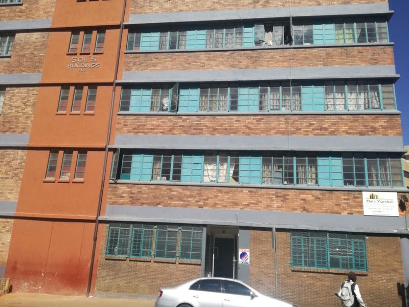 Front elevation of Sol's Buildings, a historic brick apartment building featuring multi-pane steel windows and ground-level security grilles.