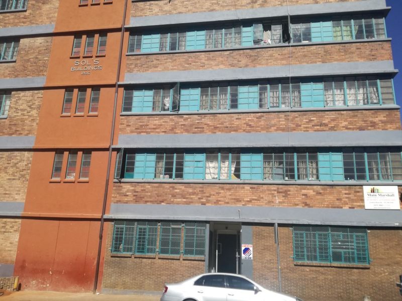 Front elevation of Sol's Buildings, a multi-story brick apartment complex featuring original steel-framed windows and ground-level security bars.