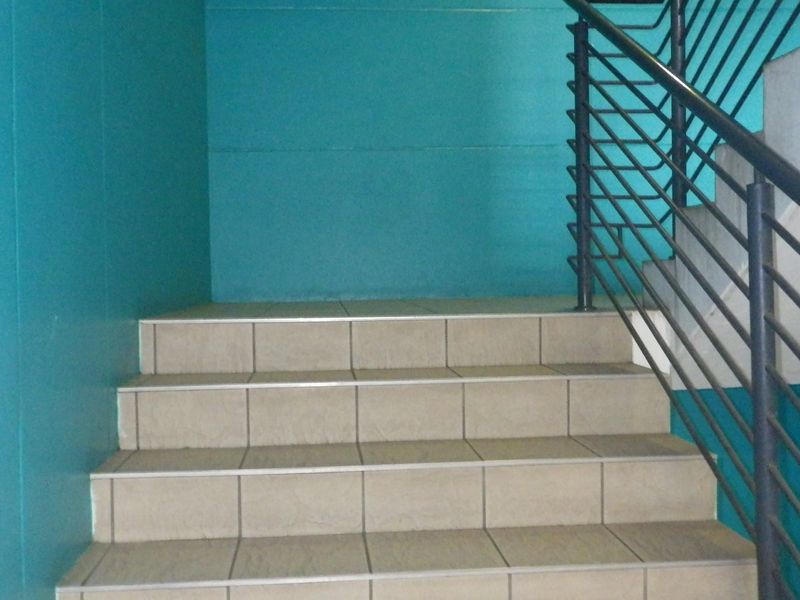 A functional indoor staircase featuring tiled steps and a sturdy metal handrail against painted walls.