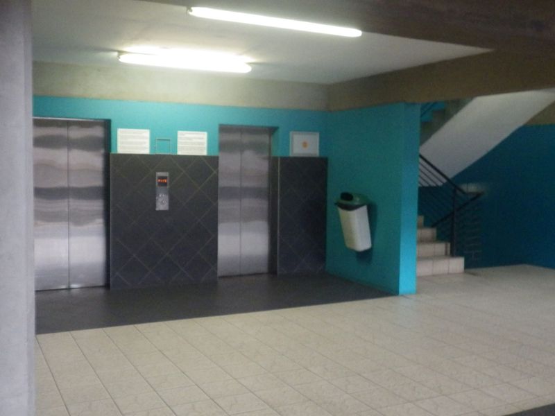 A communal building entrance lobby featuring dual elevators, a staircase, tiled flooring, and bright overhead lighting.