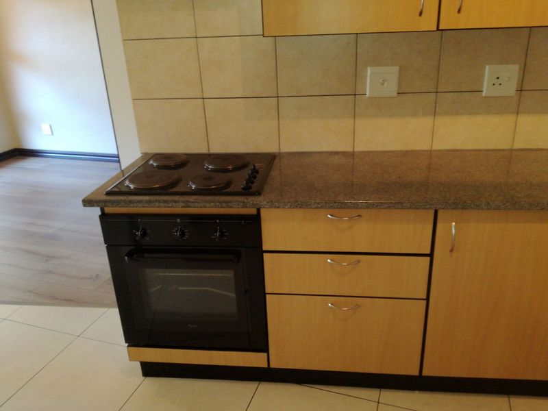 A functional kitchen area featuring light wood cabinetry, granite countertops, a built-in oven with electric hob, and neutral tiled backsplash and flooring.
