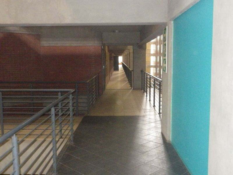 A long, open-air apartment complex hallway featuring metal balustrades, tiled flooring, and exposed concrete structural elements.