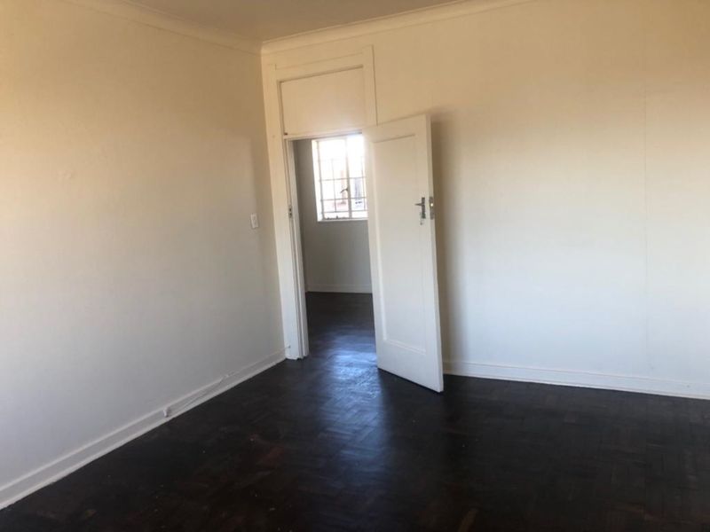 An empty bedroom featuring dark parquet flooring, white walls, and a classic internal door leading to an adjacent space.