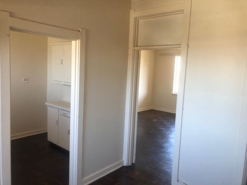A view from the hallway looking into an adjacent kitchen and bedroom, featuring original parquet flooring and classic architectural door frames.