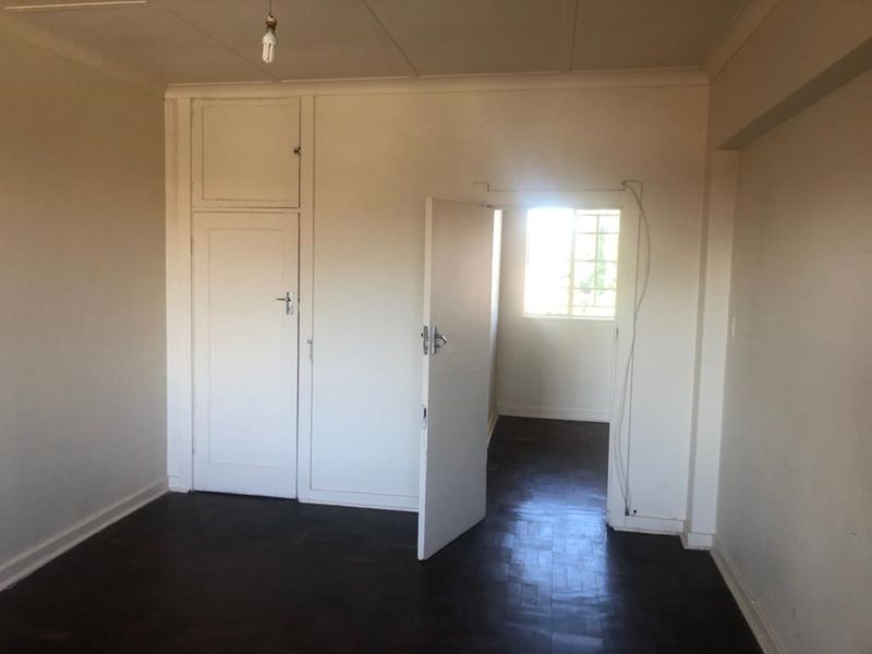 An empty bedroom featuring original parquet flooring, built-in storage cupboards, and a window with security bars.