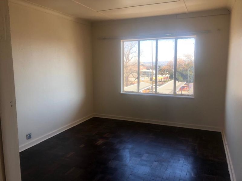 An empty bedroom featuring dark parquet flooring and a large window providing natural light and an exterior view.