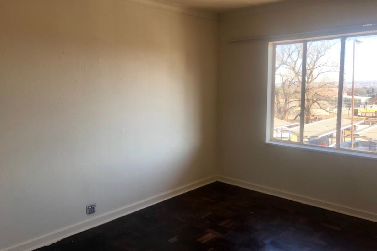 An empty bedroom featuring dark parquet flooring, neutral walls, and a large window providing natural light and an exterior view.