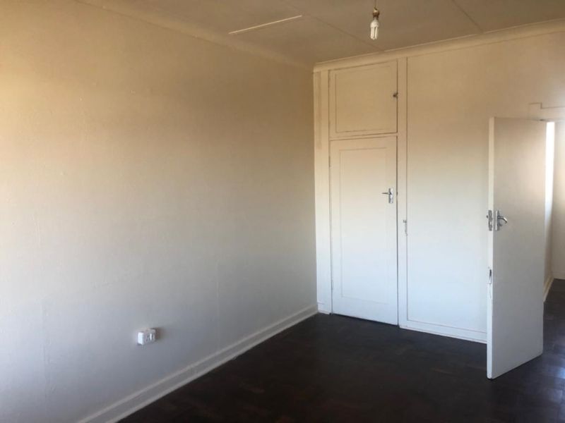 An empty bedroom featuring original parquet flooring and a built-in cupboard, offering a blank canvas for renovation or interior design updates.