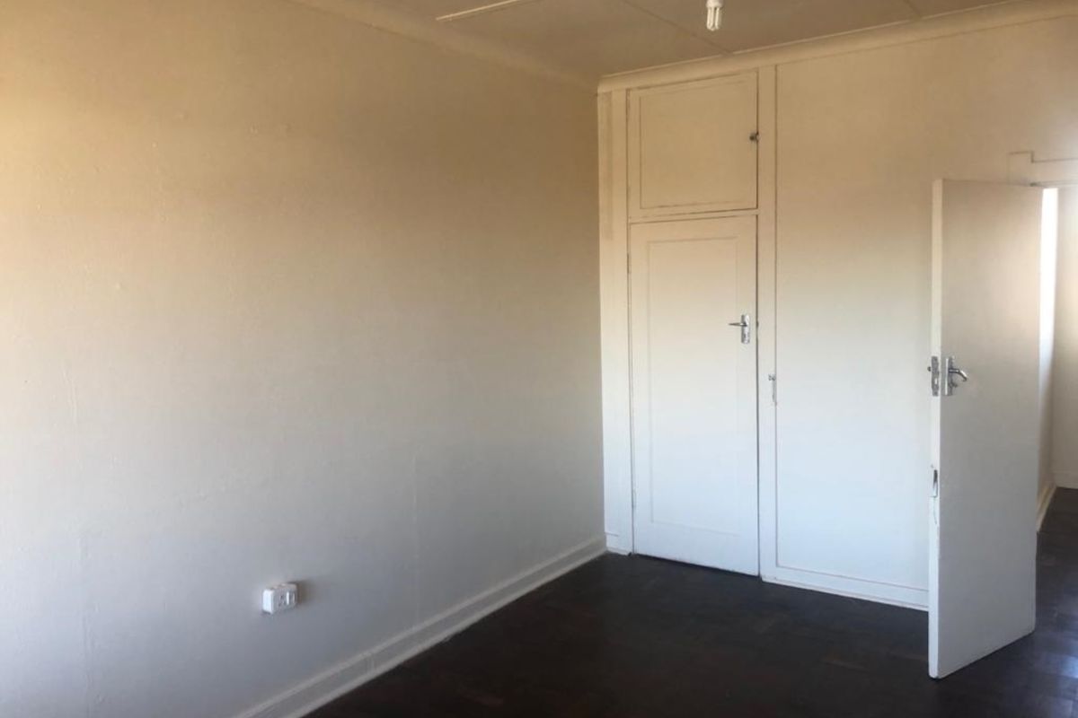 An empty bedroom featuring original parquet flooring and a built-in cupboard, offering a blank canvas for renovation or interior design updates.