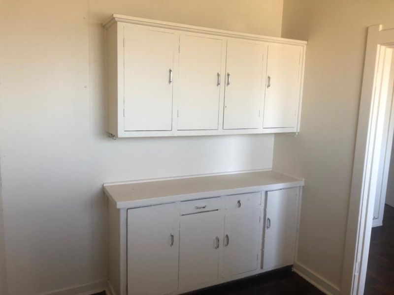 A dated kitchen area featuring original built-in white cabinetry and a laminate countertop, offering a blank canvas for potential renovation.