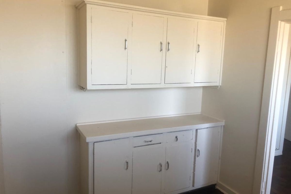 A dated kitchen area featuring original built-in white cabinetry and a laminate countertop, offering a blank canvas for potential renovation.