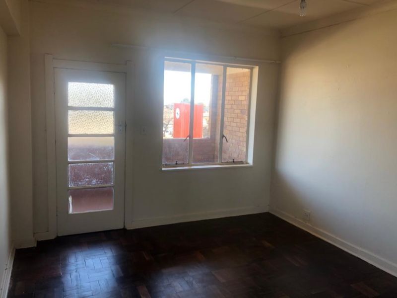An empty bedroom featuring original parquet flooring, a timber-framed window, and a glass-paneled door leading to an exterior space.