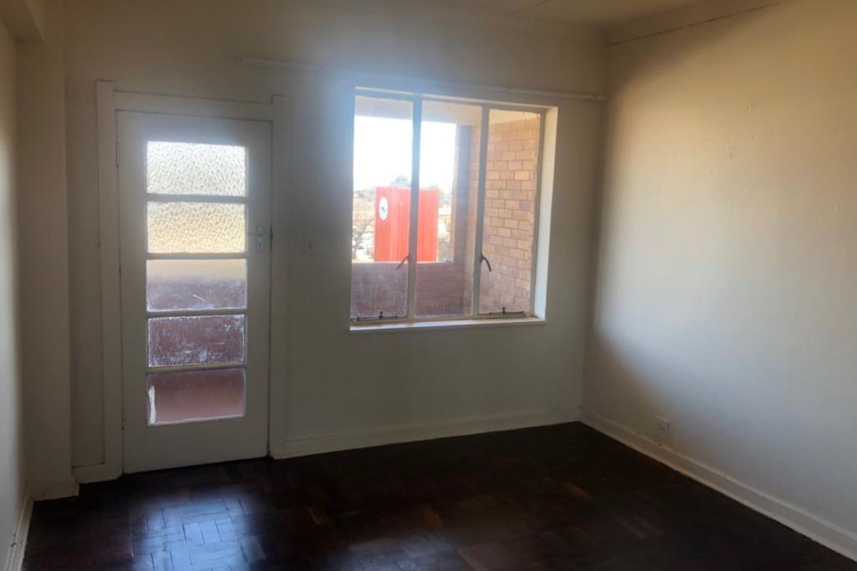 An empty bedroom featuring original parquet flooring, a timber-framed window, and a glass-paneled door leading to an exterior space.
